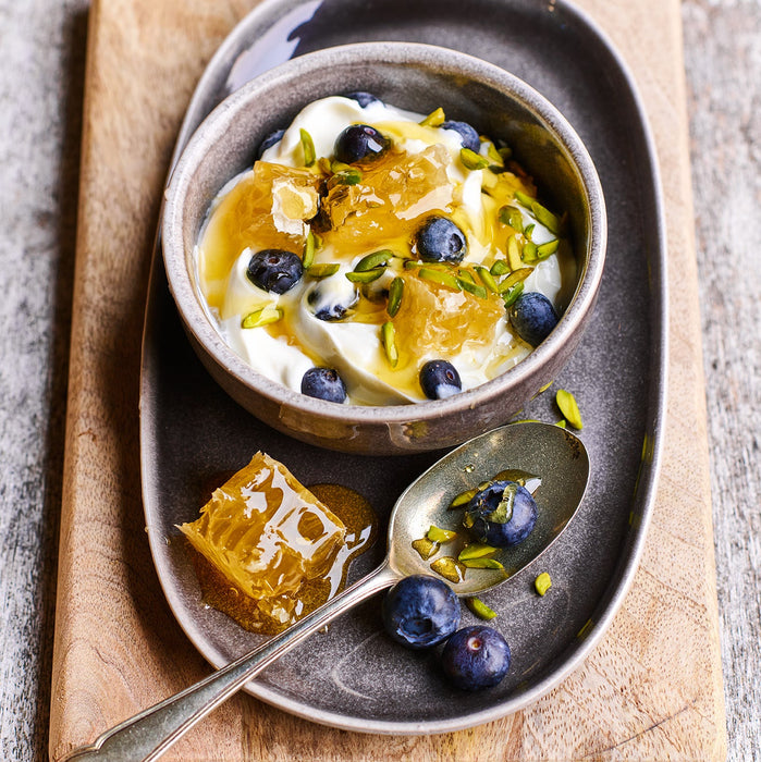 Dessert with yogurt, honeycomb, and blueberries on a wooden board.