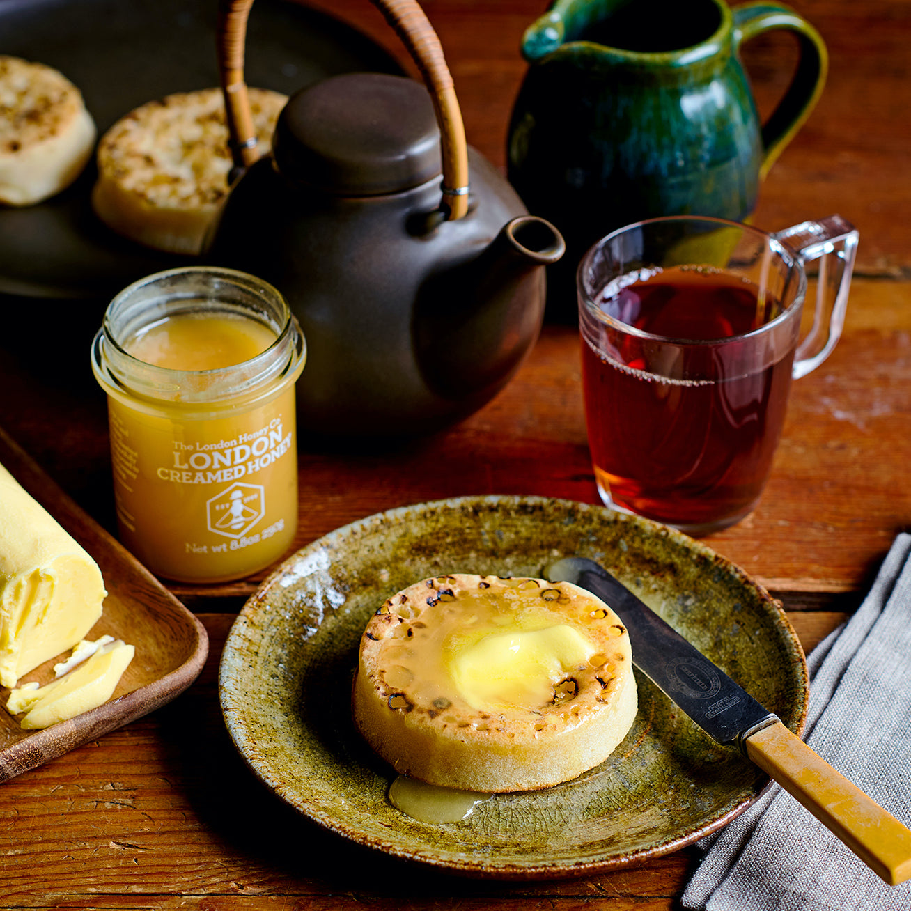 Tea time setting with warm crumpets, real British honey, and tea on a wooden table.